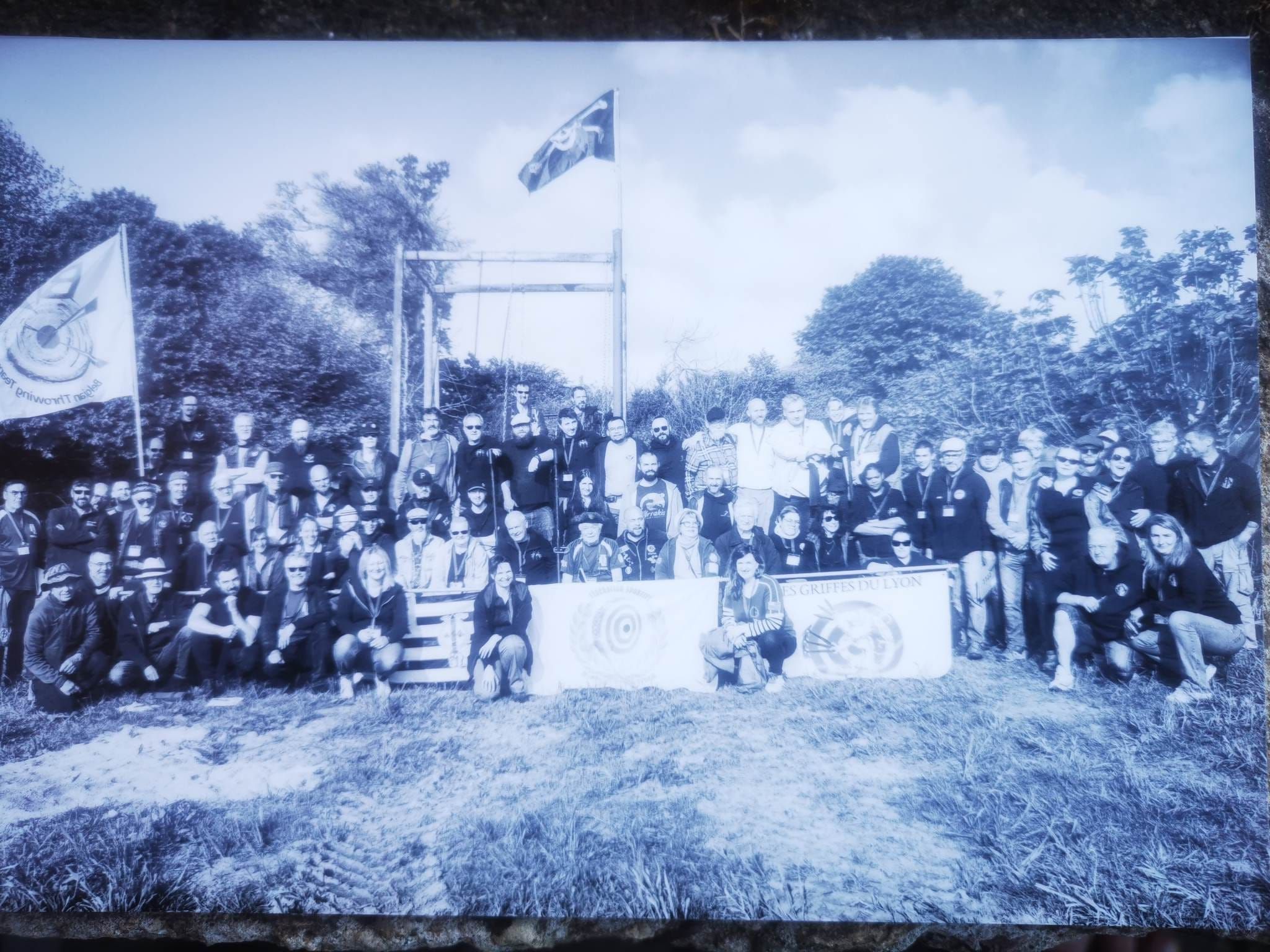 Photo d'archive en noir et blanc : un grand groupe réuni en plein air autour d'une banderole.