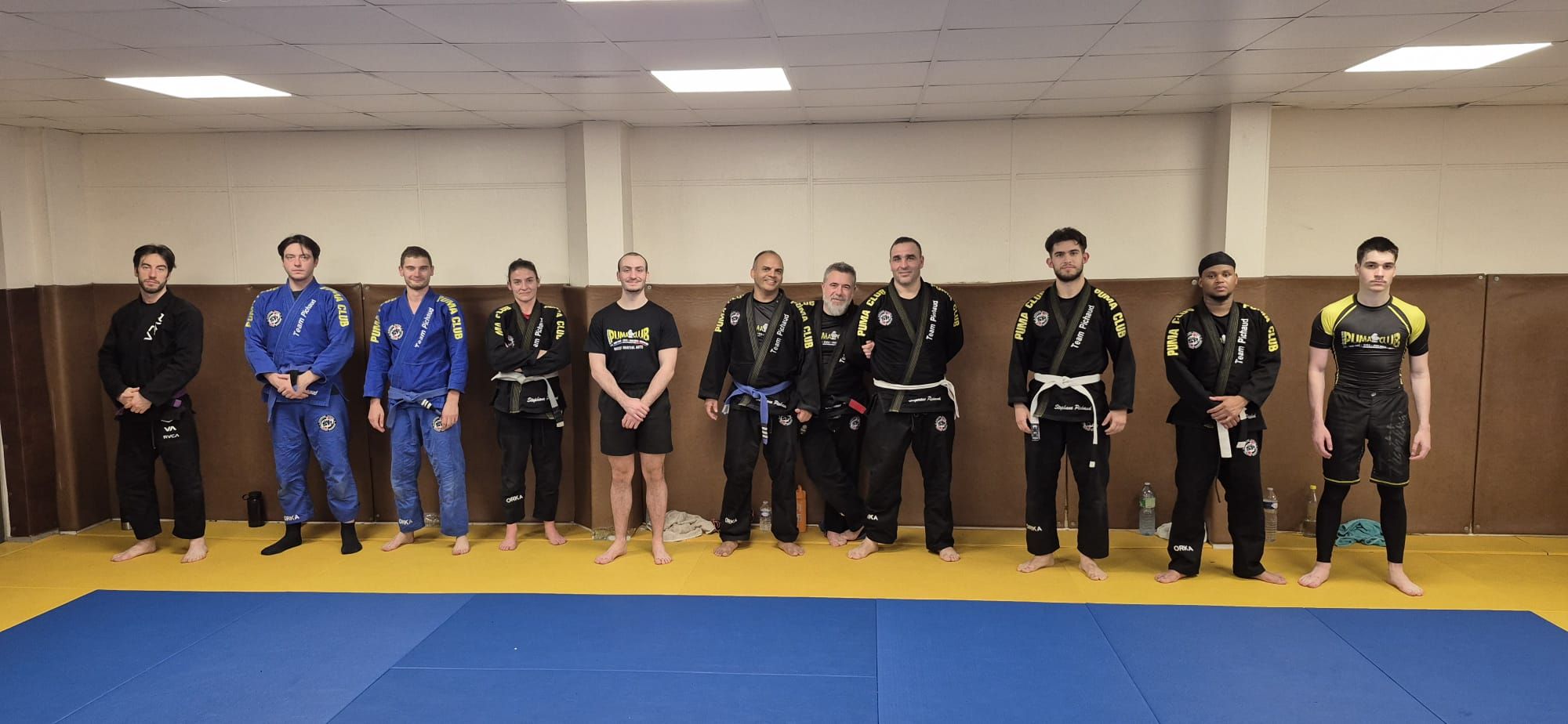 Pratiquants alignés sur le tatami, en kimono et en tenue de grappling.